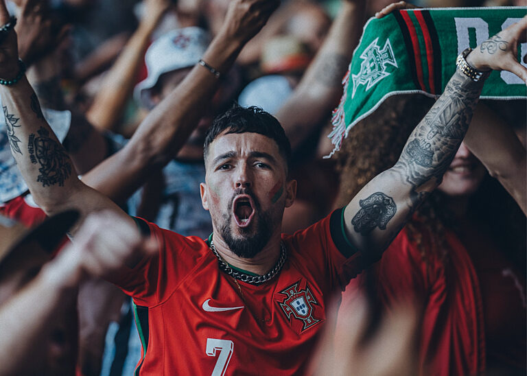 Jubelnder Fußballfan im roten Portugal-Trikot mit erhobenem Schal inmitten einer begeisterten Menge.